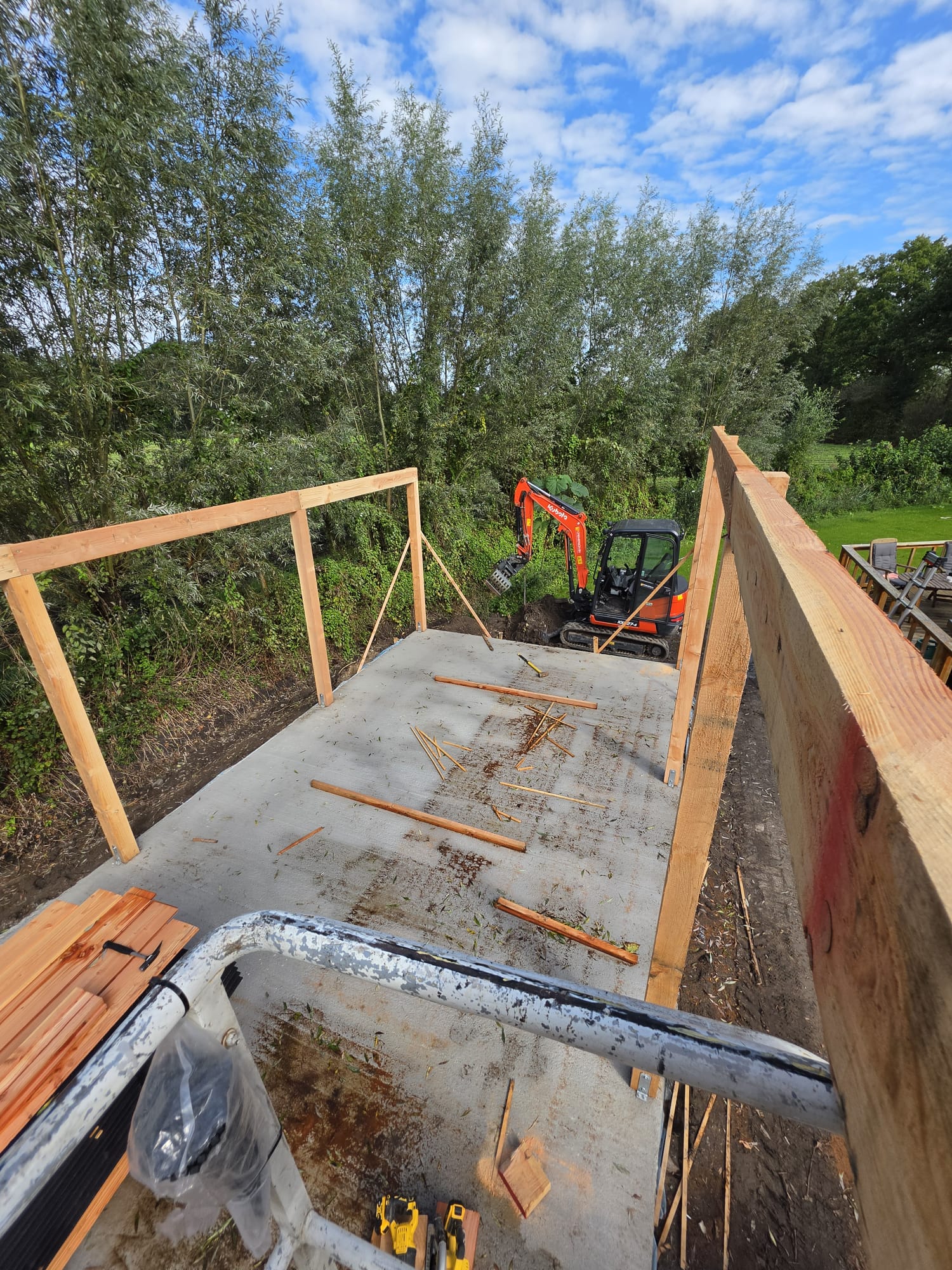 Fundering met houten stijlen en minigraver op de bouwplaats van de houten schuur