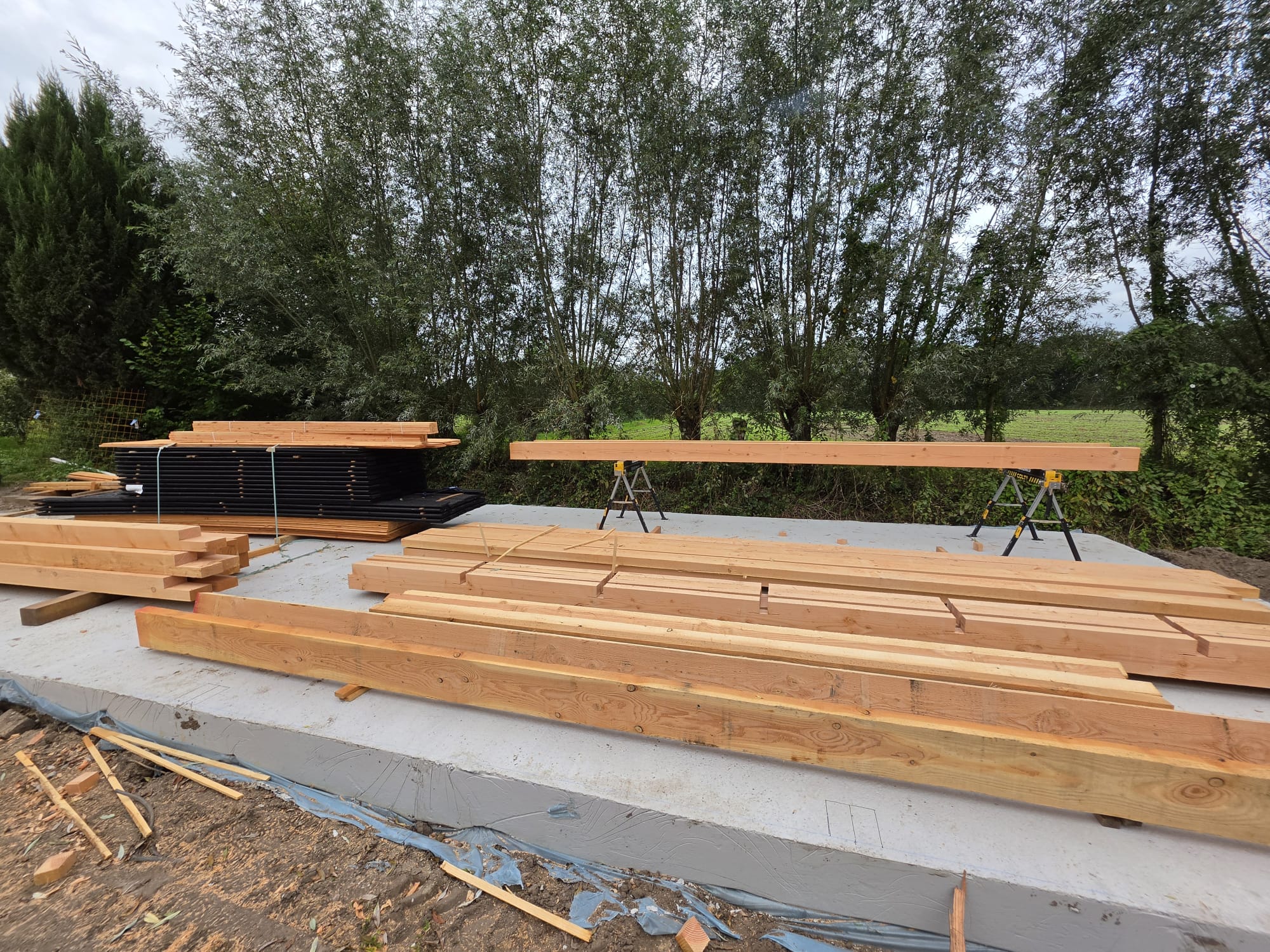 Houten liggers en dakpanplaten opgestapeld op de fundering van de schuur